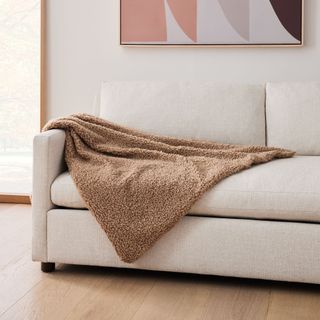 A West Elm Cozy Faux Shearling Throw in a sable on a sofa