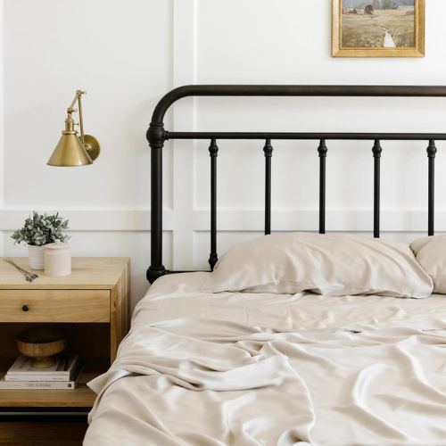 Close up of bed with black metal frame, cream sheets, wooden side table, small artwork above bed