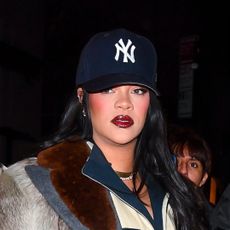 Rihanna in Manhattan on January 17, 2026 wearing a Prada fur coat, Loewe two tone boots, a black skirt, a casual track jacket, and a baseball cap