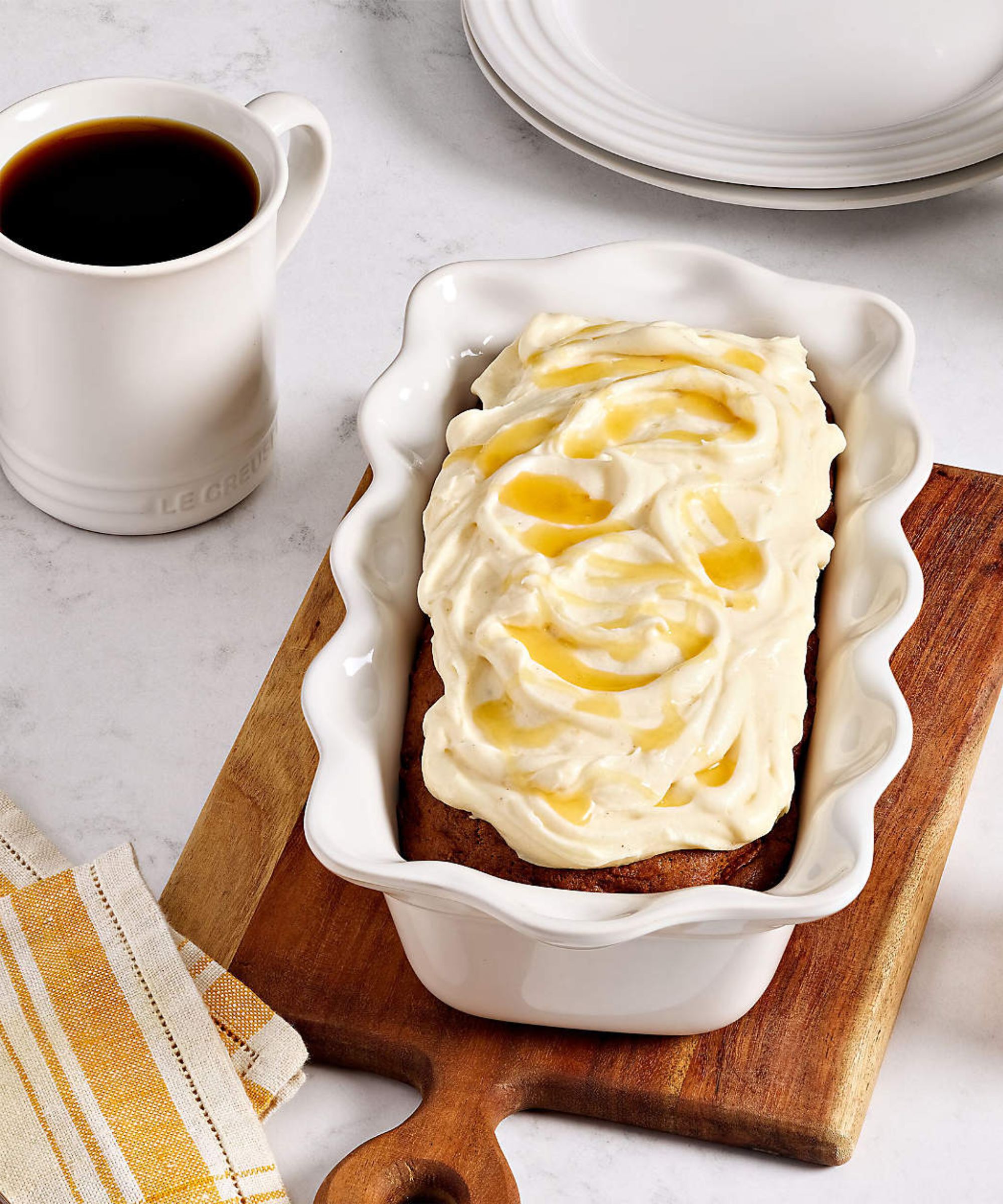 Cake in fluted white loaf dish on chopping board next to white Le Creuset mug