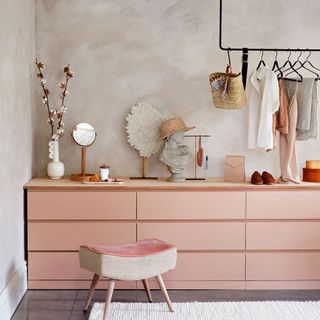 Dressing room with black clothes hanging rail above pink drawers