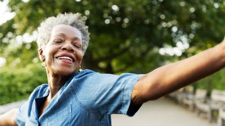 An older woman closes her eyes, smiles and lifts her arms out in happiness.