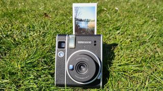 En Fujifilm Instax Mini 40 ligger på en gräsmatta med en utskrift färdig på toppen av kameran.