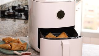 air fryer on a kitchen counter top with samosas inside, and on a plate to the side