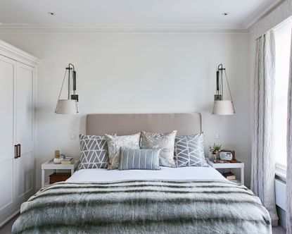 A grey bed with cushions in neutral greys and beiges in front of two large wall lights