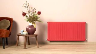 Red painted radiator in room with wooden floor, chair, and table with plant on