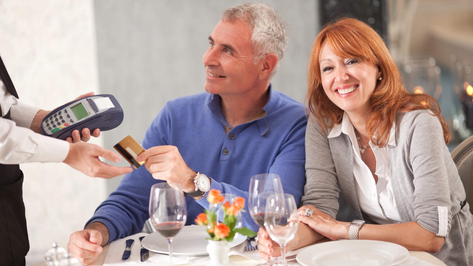 Cheerful mature couple paying for dinner in restaurant with credit card