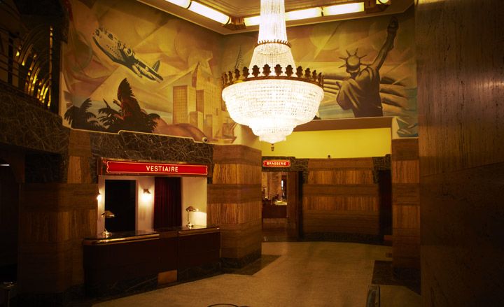 A lobby with a reception counter, large chandelier, artistically painted walls and marble floors.