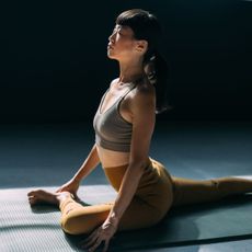 A woman doing yoga on a green workout mat, in a sunlit studio