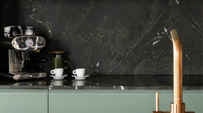 Close-up image of a green marble kitchen countertop with an espresso maker and two espresso cups on it.