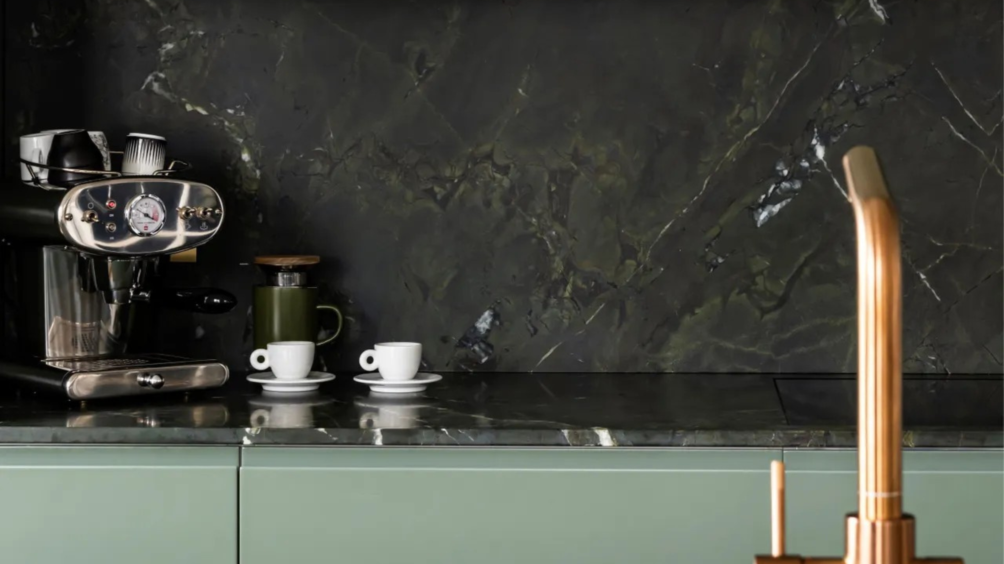 Close-up image of a green marble kitchen countertop with an espresso maker and two espresso cups on it.