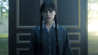 Wednesday in her PJs walking outside with a door behind her