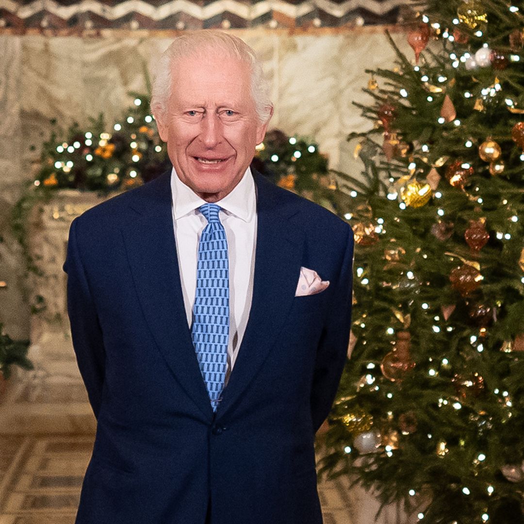 King Charles standing in front of a Christmas tree in a blue suit and tie