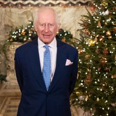 King Charles standing in front of a Christmas tree in a blue suit and tie
