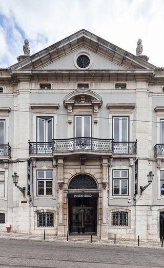Outside look at the Palacio Chiado. An older-looking, gray building that's set on the street that's set on a hill.