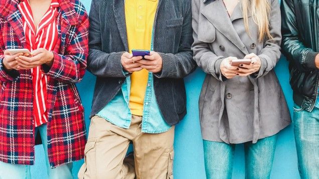 A lineup of people using their smartphones against a blue wall