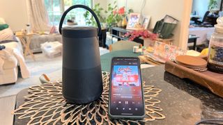 Bose speaker on a table next to a smartphone with a living room scene in the background