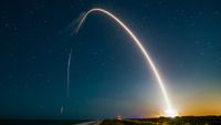 a spacex rocket carves an orange-white arc into the night sky during a launch
