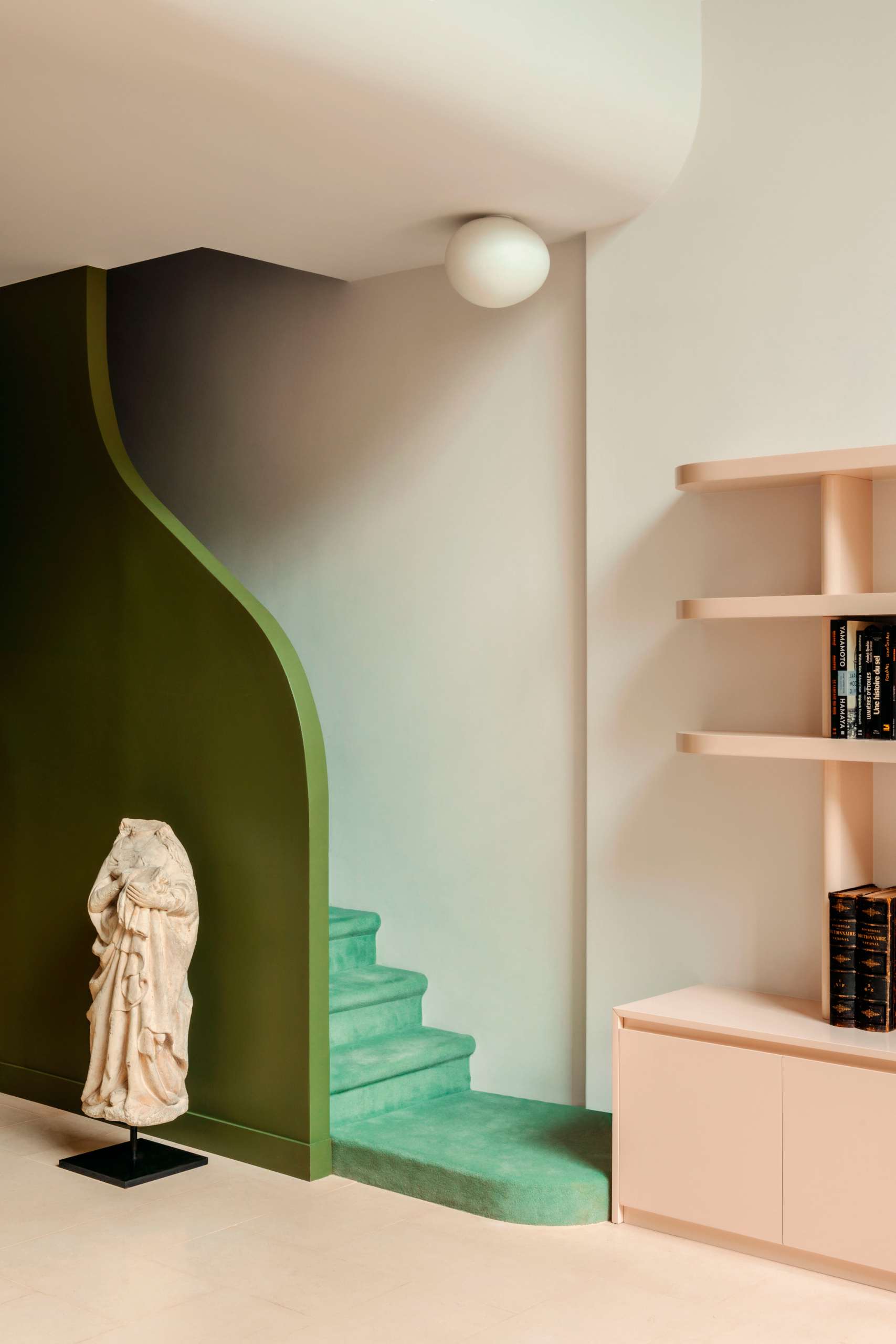 Staircase with curved green stair wall, green carpet, leading to a peachy pink storage unit