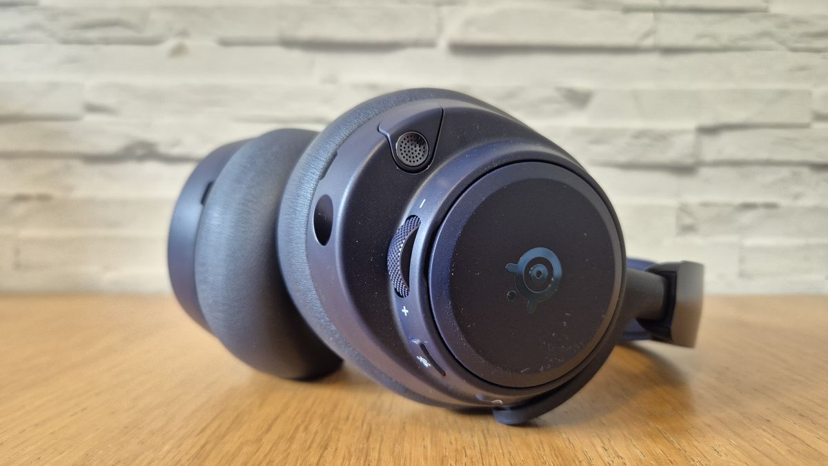 The SteelSeries Arctis Nova Pro Omni in front of a white brick background and on a wooden surface.