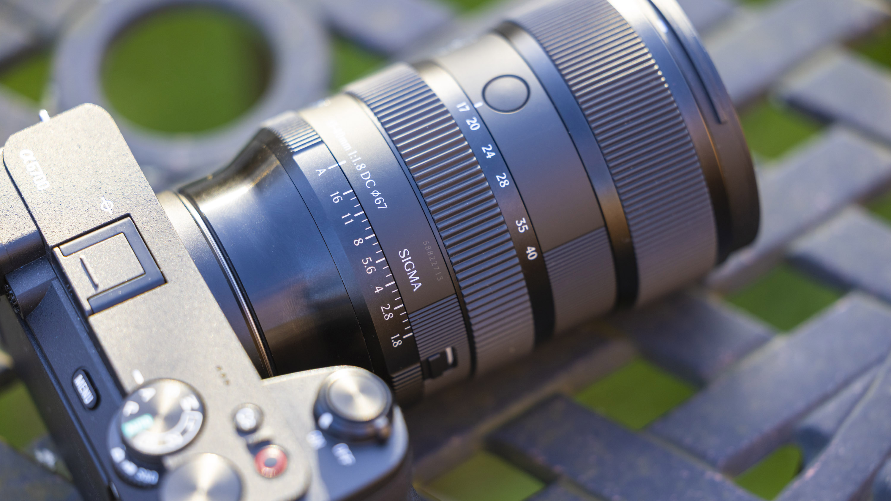 Sigma 17-40mm f1.8 DC Art lens product shot taken outdoors on a metal garden table with blurry bokeh background