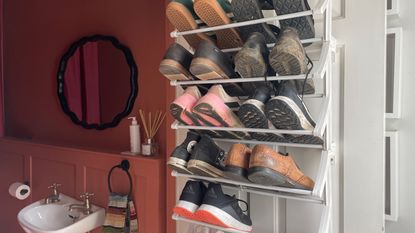 white door with a white shelving rack holding shoes and trainers with a glimpse of a red bathroom behind