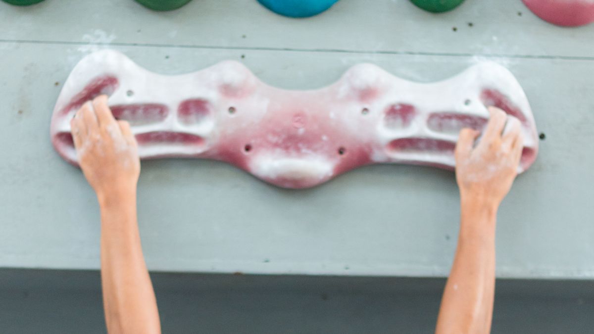 Close up of a woman&#039;s hands hanging from a hangboard