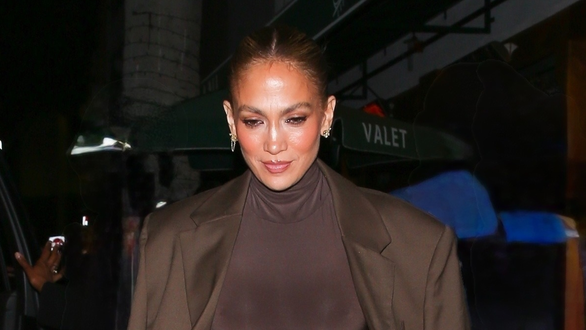 Jennifer Lopez wears a brown dress and matching jacket, carries a furry clutch, and wears peep-toe platforms
