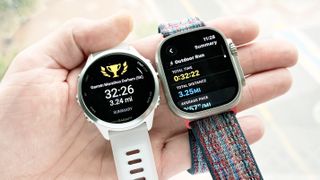 Close-up of the Garmin Forerunner 570 and Apple Watch Ultra 3 in the writer's hand showing the results of a 5K run
