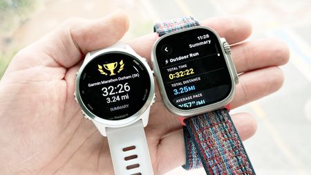 Close-up of the Garmin Forerunner 570 and Apple Watch Ultra 3 in the writer's hand showing the results of a 5K run