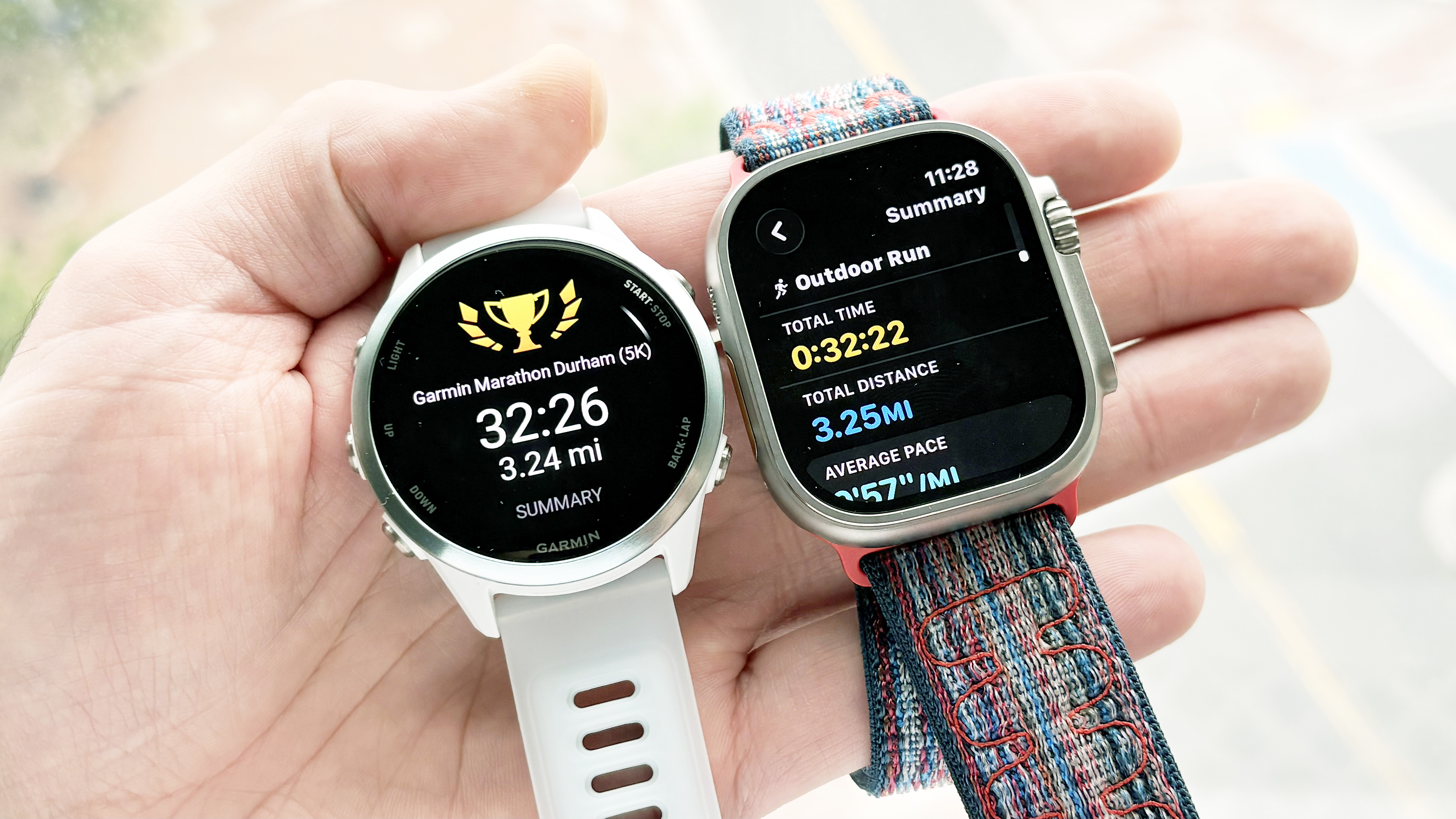 Close-up of the Garmin Forerunner 570 and Apple Watch Ultra 3 in the writer's hand showing the results of a 5K run