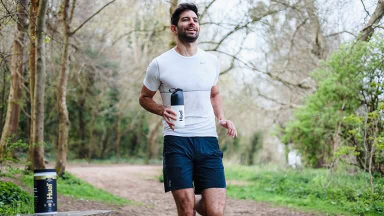 Person running in a forest carrying a Huel protein shaker