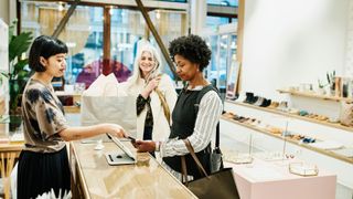 Woman paying with smartphone after shopping in boutique with friend