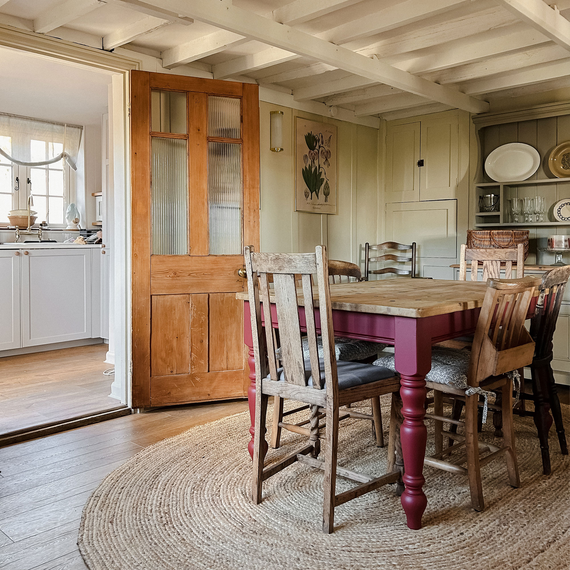 Wooden dining set on oval woven rug in room with white painted ceiling beams