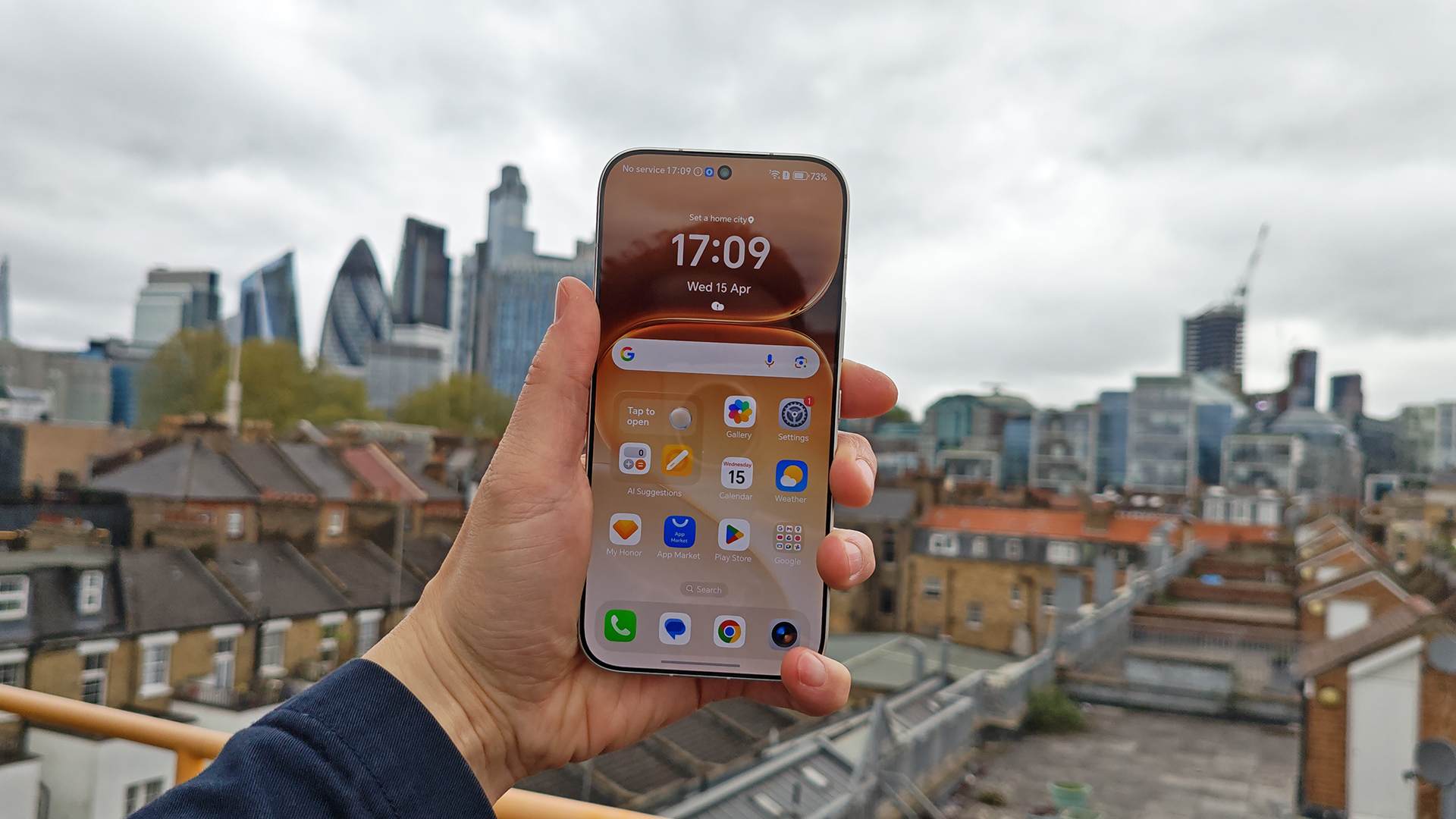 A hand holding an illuminated Honor 600 Pro smartphone displaying its home screen, with a cityscape and London skyline blurred in the background.