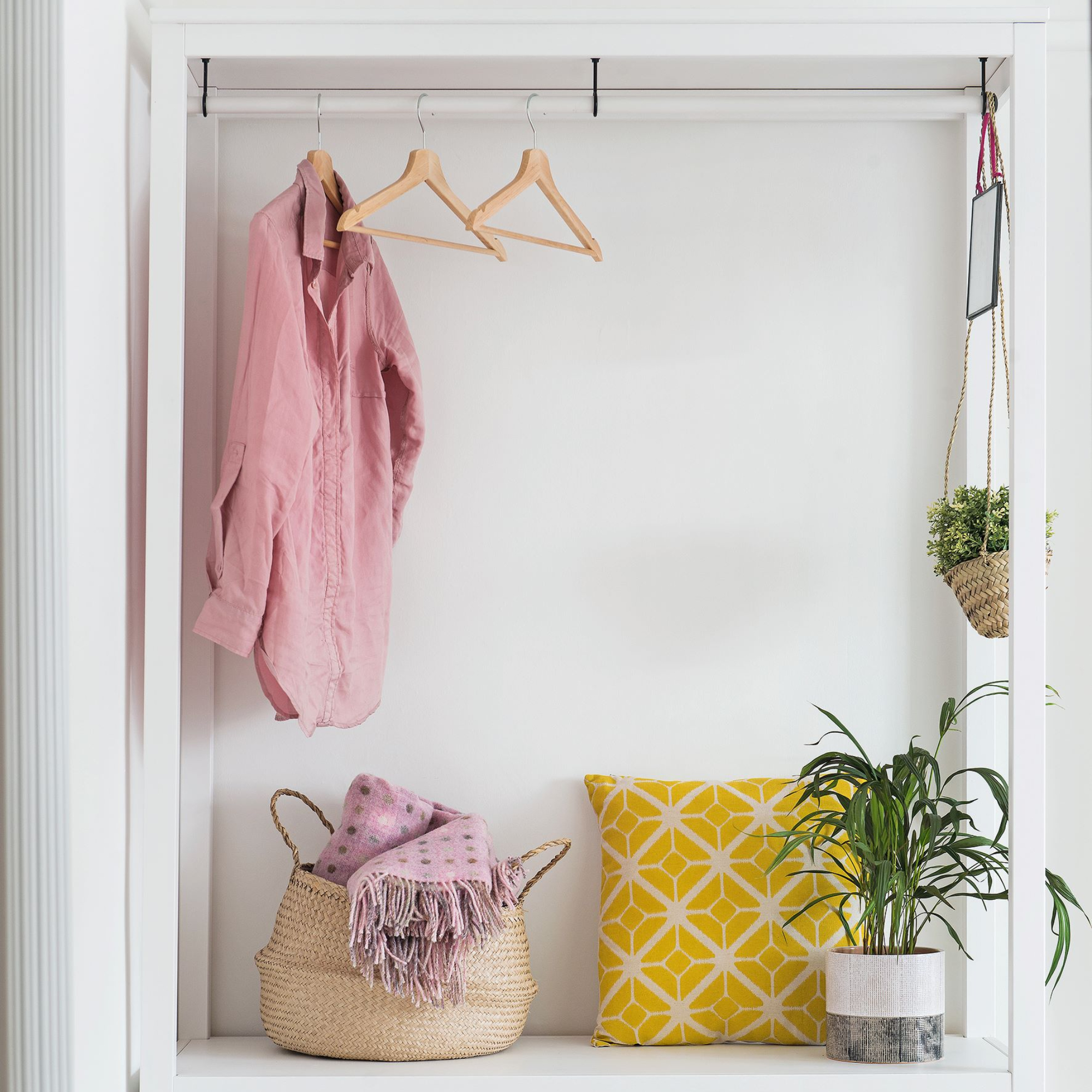 White storage unit with cabinets and hanging rail against white wall, with plants and objects in green, yellow, pink, and white