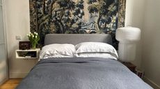 Pottery Barn navy Linen Bedding on bed with white cushions, tapestry above bed, paper lantern on one bedside, and a floating bedside on the other with a picture frame and vase of tulips
