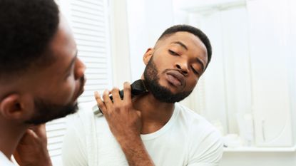 A man looking in a bathroom mirror, trimming his beard using one of the best beard trimmers
