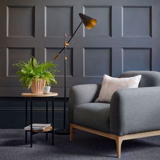 blue panel wall with grey sofa chair and cushion plant vase on table and lamp