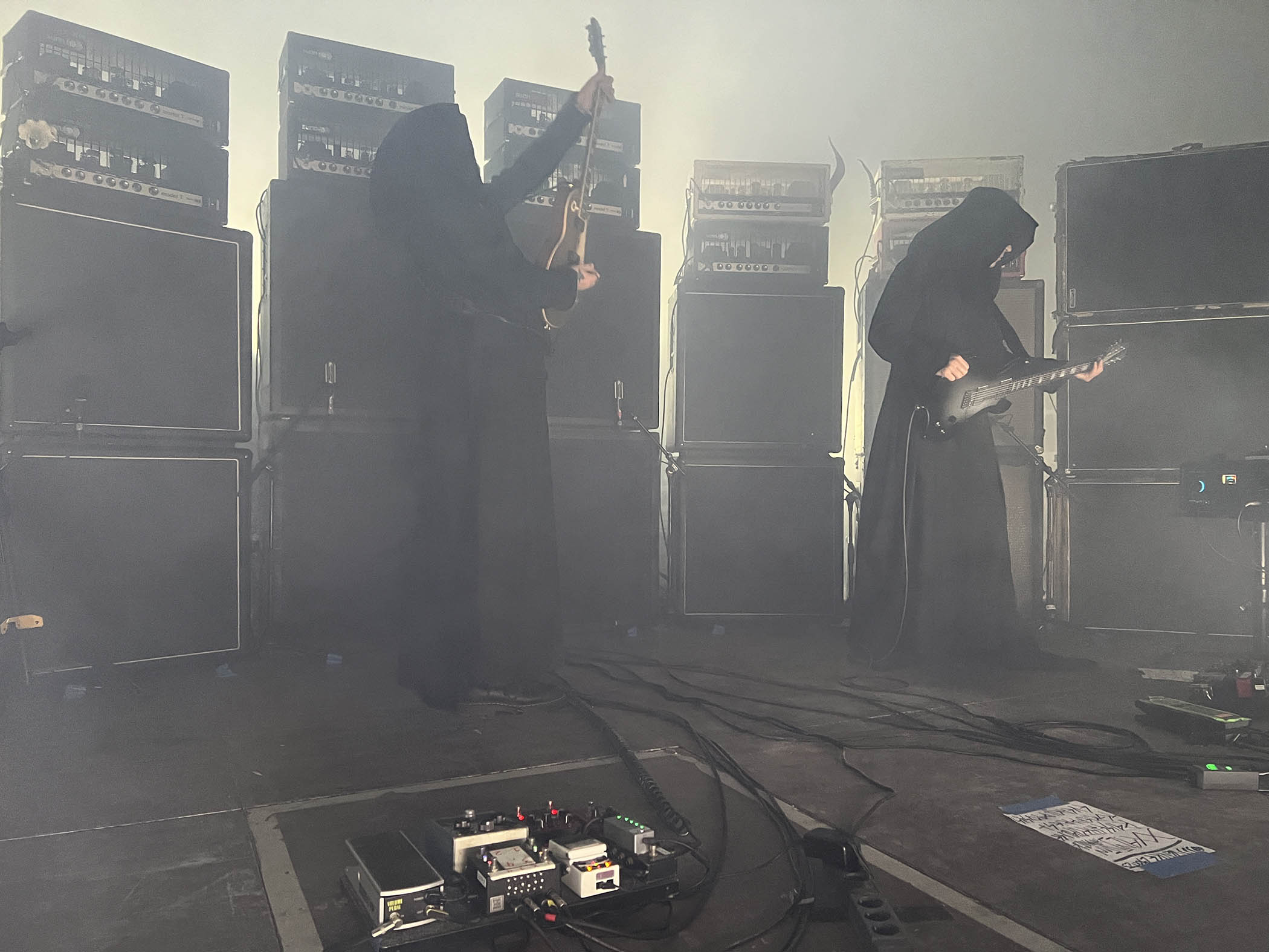 Greg Anderson and Stephen O'Malley of Sunn O))) wear cowls as they perform live in front of banks of high-powered tube amps.