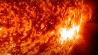 closeup shot of a bright white flare erupting from the sun's mottled orange surface