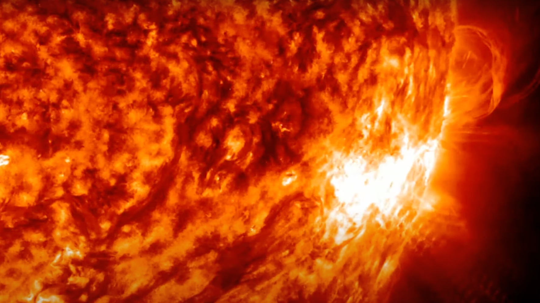 Close-up shot of a bright white glow erupting from the sun's mottled orange surface