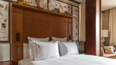 A hotel bed with a tall headboard and a painted map on the wall