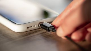 A person&#039;s hand plugs a phone cable into a smartphone.