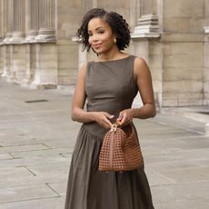 Woman on street wears dark brown dress, carried brown woven handbag