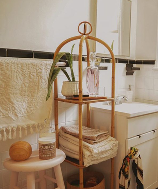 Cane tiered bathroom caddy with folded towels and potted plant in white relaxed small bathroom