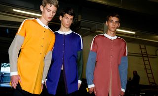 Three guys wearing the JW Anderson S/S 2015 collection. They are all wearing the same style shirt with a white collar. The first guy is wearing a yellow and beige shirt. The middle guy is wearing a blue and green shirt and the guy on the right is wearing red and blue shirt.