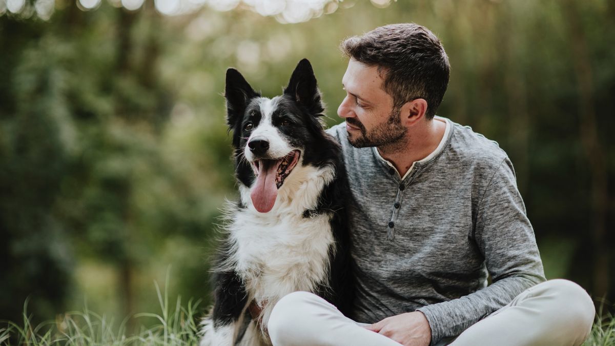 Man smiling and looking at his dog while they sit in the park