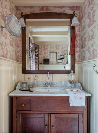 dark wood bathroom vanity unit and mirror with toile de Jouy wallpaper