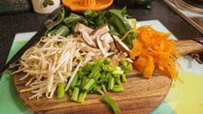 Chopped ingredients presented on a cutting board. Pak choi, beansprouts, shredded carrot, shitake mushrooms and spring onion.